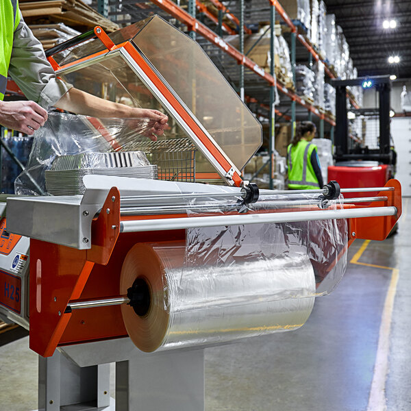 A person in a green vest using a machine to wrap plastic bags in Lavex Pro shrink film.