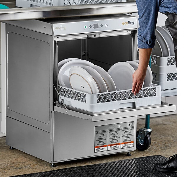 A person standing next to an open Ecoline by Hobart undercounter dishwasher, putting white plates in the dishwasher.