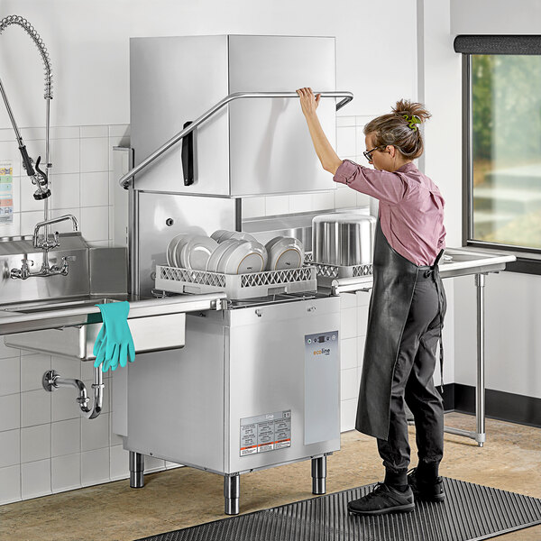A woman in a black apron loading plates into an Ecoline by Hobart electric door-type dishwasher on a counter in a professional kitchen.
