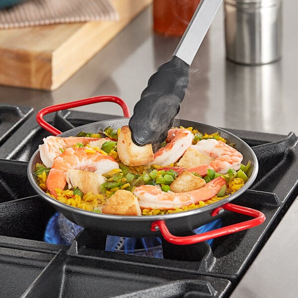 A Vigor carbon steel paella pan filled with shrimp and vegetables cooking on a stove.