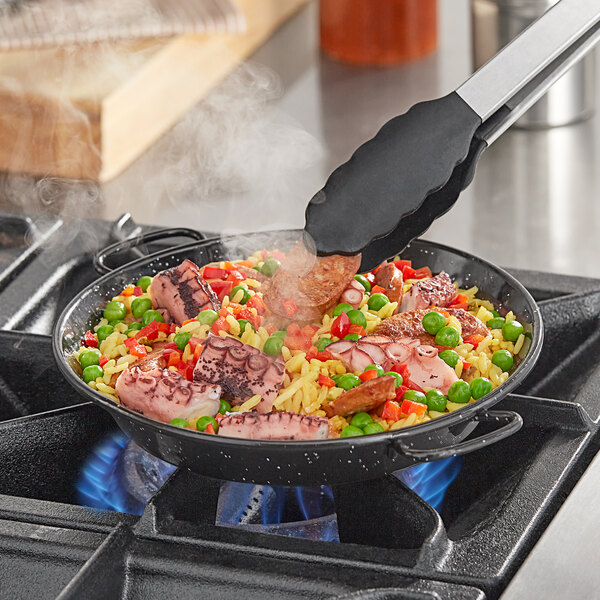 A Vigor enameled carbon steel paella pan of food cooking on a stove.