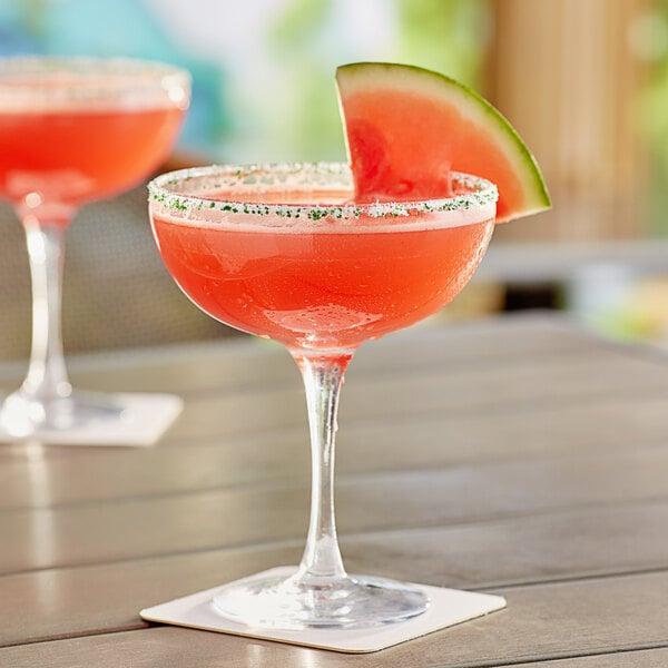 Two Acopa margarita glasses filled with red drinks on a table with watermelon garnish.