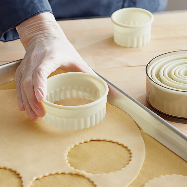A person using a Mercer Culinary round fluted cutter to cut pie dough.