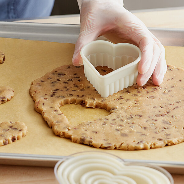 A person using a Mercer Culinary heart shaped cookie cutter to cut heart shapes from cookie dough.