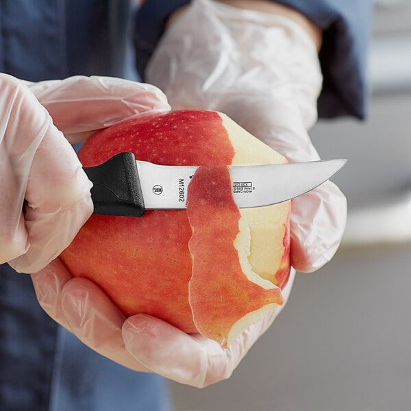 A person in gloves using a Mercer Culinary peeling knife to peel an apple.