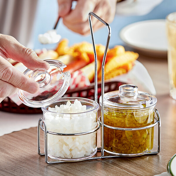 A person pouring green sauce into a clear glass container with a lid using a Choice wire condiment caddy.