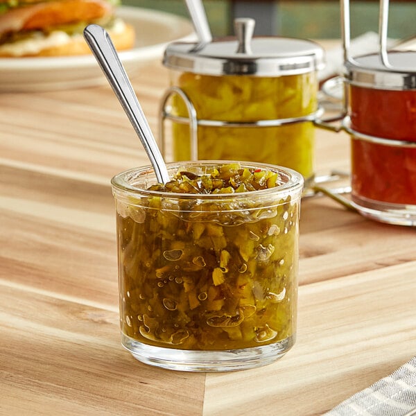 A glass jar of green relish with a spoon inside.