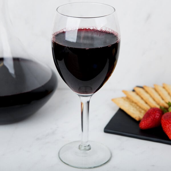 A Libbey Vino Grande wine glass filled with red wine next to a tray of strawberries.