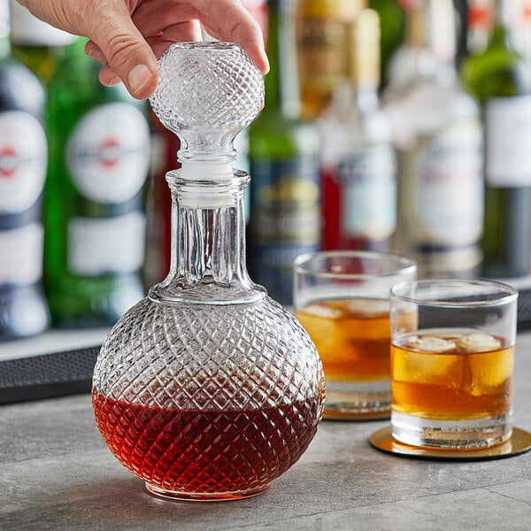 A hand pouring amber liquid into an Acopa Cut Glass Whiskey Decanter.