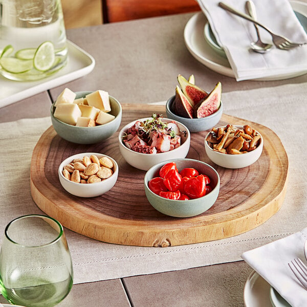 An Acopa acacia wood serving board with bowls of food and a glass with a green rim on a table.