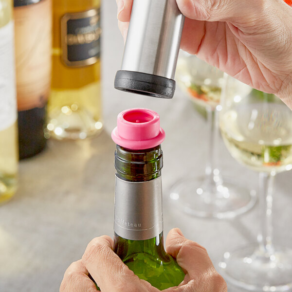 A hand using an Acopa pink vacuum wine stopper to seal a bottle of wine.