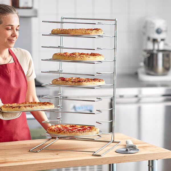 A woman wearing a red apron holding a tray of pizzas on a Choice oversized pizza pan rack.