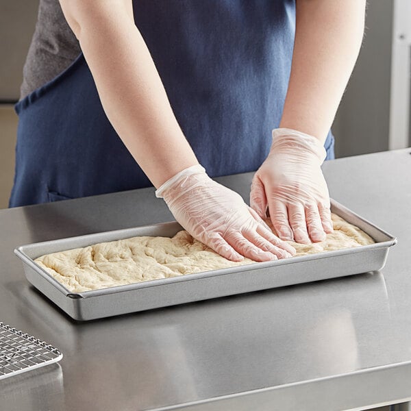 A person wearing gloves making dough in a Chicago Metallic hot dog bun pan.