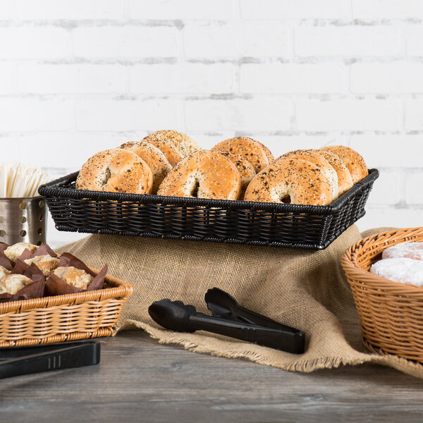 A black rectangular plastic basket filled with bagels and pastries on a table.