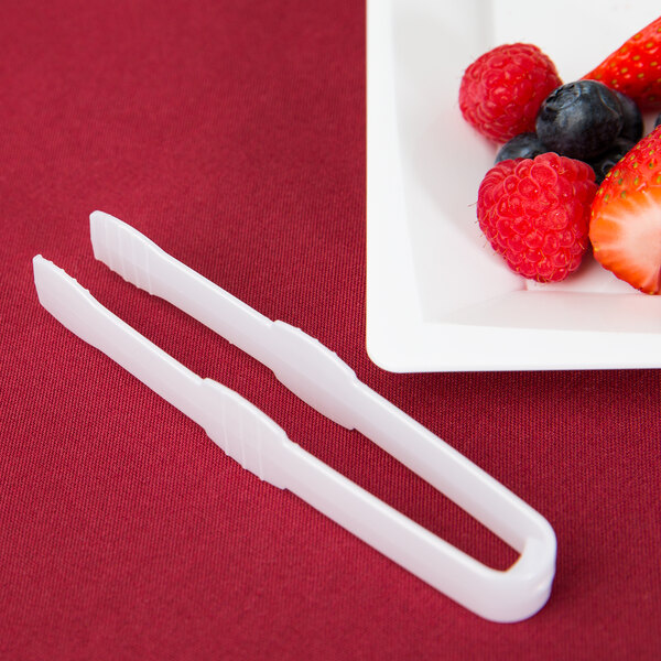 A white plate of fruit with Fineline white plastic tongs.