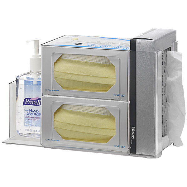An Omnimed clear acrylic infection prevention station with sanitizer section holding two bottles of hand sanitizer.