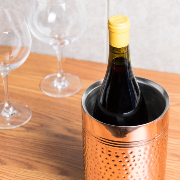 A bottle of wine in a copper metal wine cooler on a table.