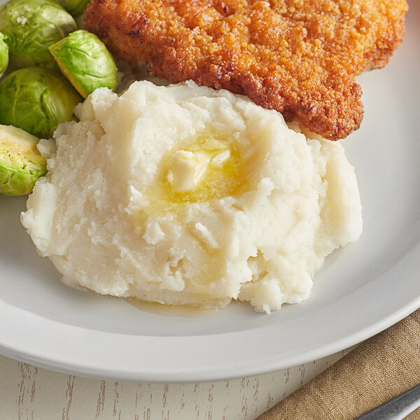 A plate of mashed potatoes with butter next to fried chicken.