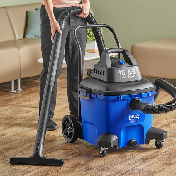 A woman using a blue and black Lavex Pro wet/dry vacuum to clean a professional kitchen.