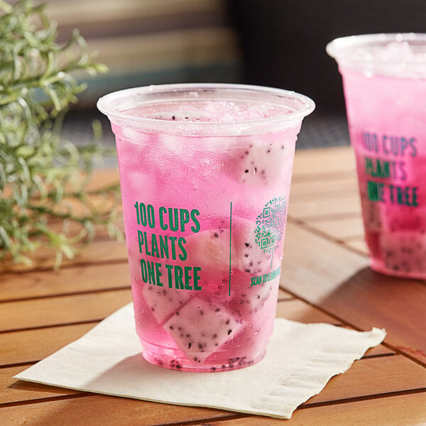 Two New Roots PLA compostable plastic cups filled with pink drinks and ice on a wooden table.