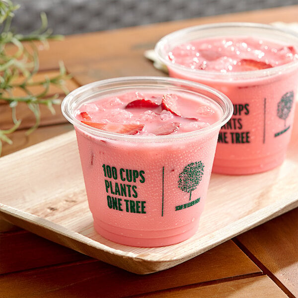 Two New Roots PLA compostable plastic cups filled with pink drinks on a wooden tray.