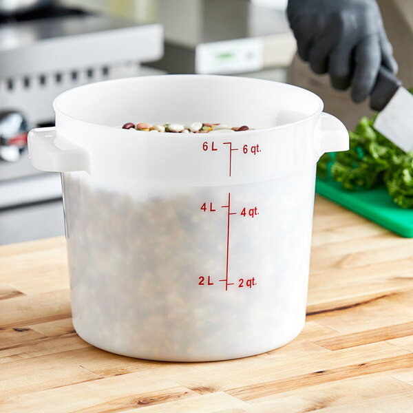 A person measuring food into a white Carlisle food storage container with a measuring cup.