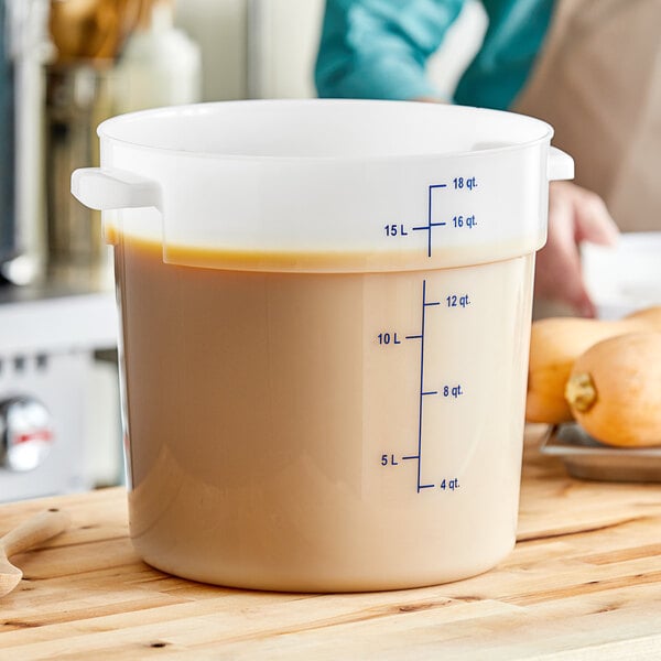 A woman using a Carlisle white food storage container to hold brown liquid from a measuring cup.