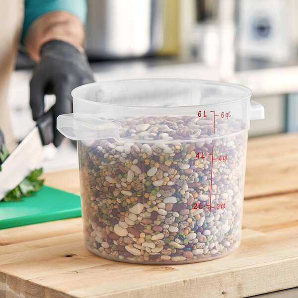 A black-gloved hand using a knife to cut vegetables in a Carlisle translucent plastic food storage container with beans in it.