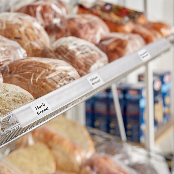 A clear clip-on label holder on a shelf with plastic-wrapped bread.