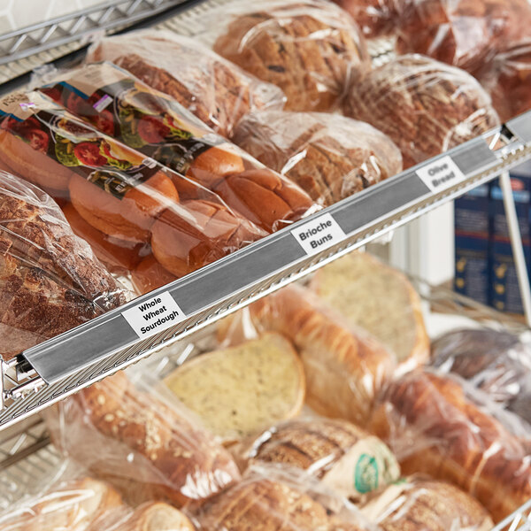 A gray clip-on label holder on a shelf with plastic bags of bread.