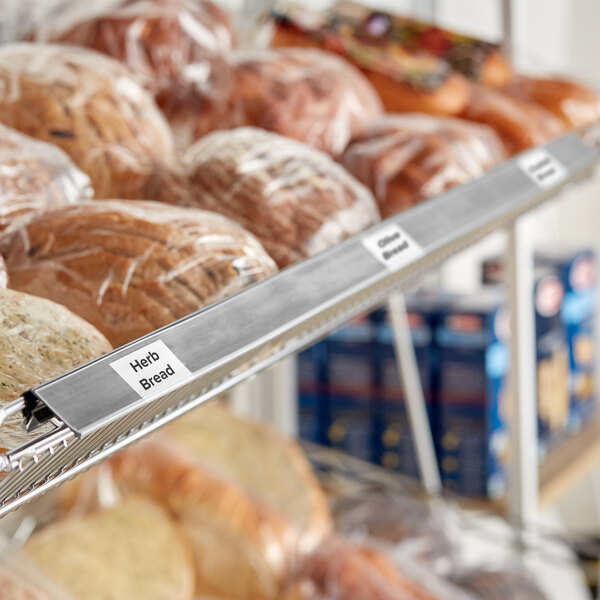 A shelf with plastic-wrapped bread on it with gray clip-on label holders.