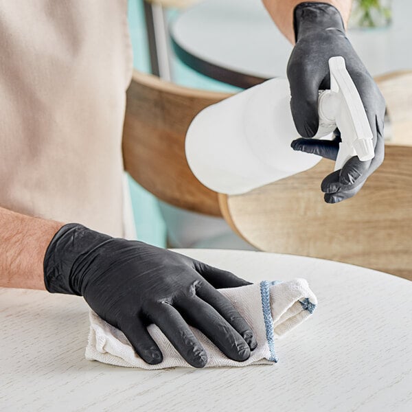 A person wearing Showa black nitrile gloves cleaning a table.
