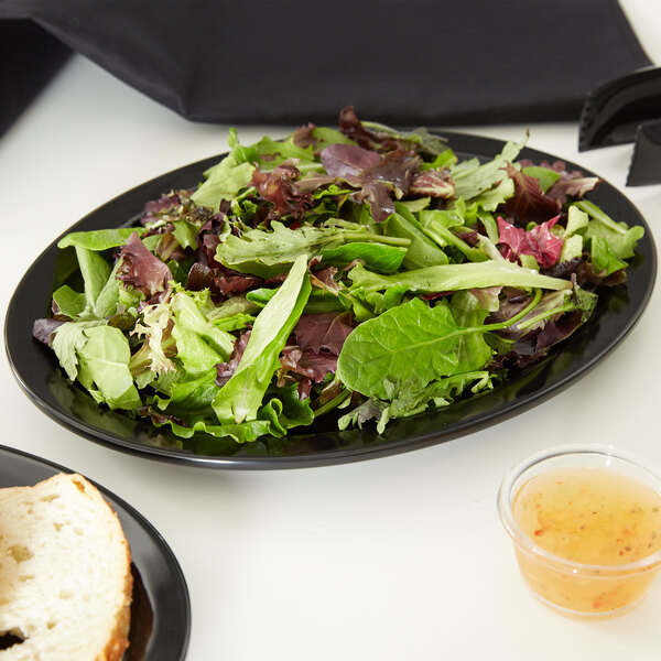 A black oval melamine platter with salad and bread on a table.