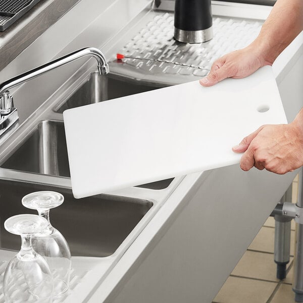 A person holding a white board over a sink in a professional kitchen.