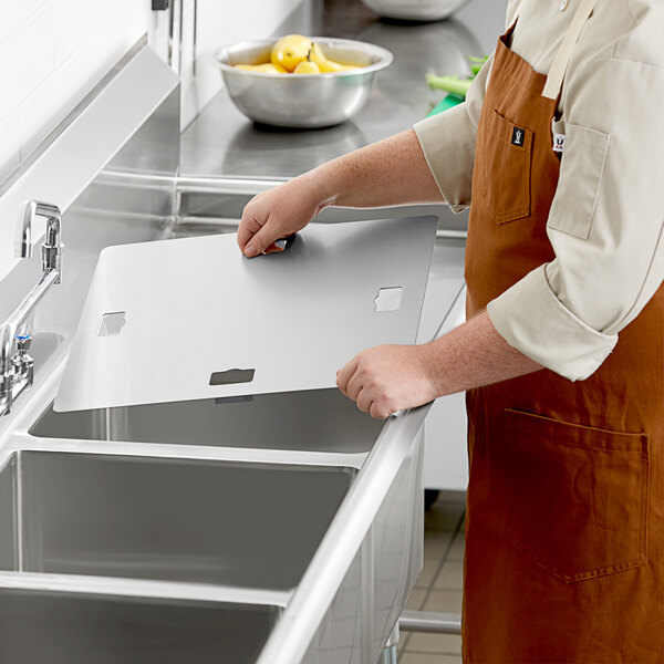 A person in an apron standing at a sink with a white box on the counter.
