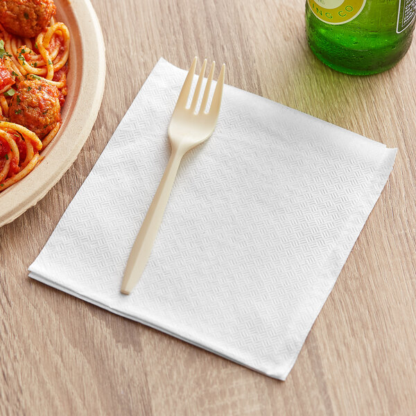 A white napkin with a fork on it next to a plate of spaghetti and a bottle of beer.