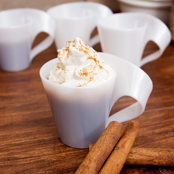 A white Fineline Tiny Tonics cup of hot chocolate with whipped cream and cinnamon sticks.
