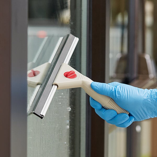A hand in a blue glove using a Lavex white plastic window squeegee to clean a window.