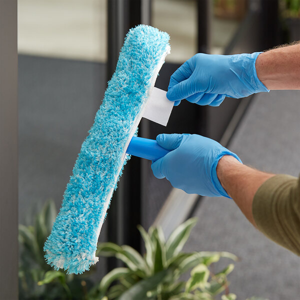 A person wearing blue gloves using a Lavex blue strip washer to clean a window.