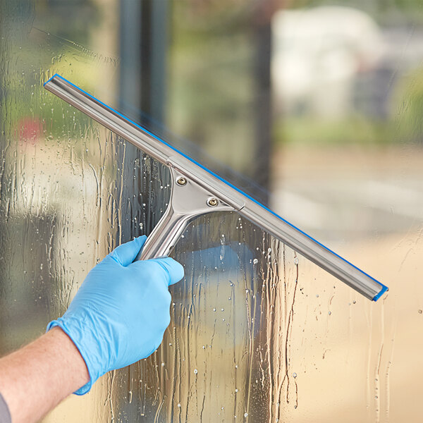 A person in blue gloves cleaning a window with a Lavex 16" Window Squeegee.