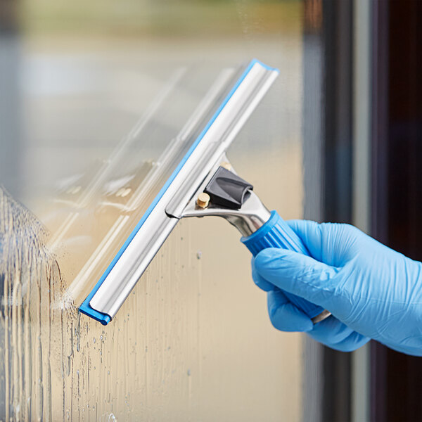 A person wearing a blue glove using the Lavex Pro window cleaning kit to clean a window.