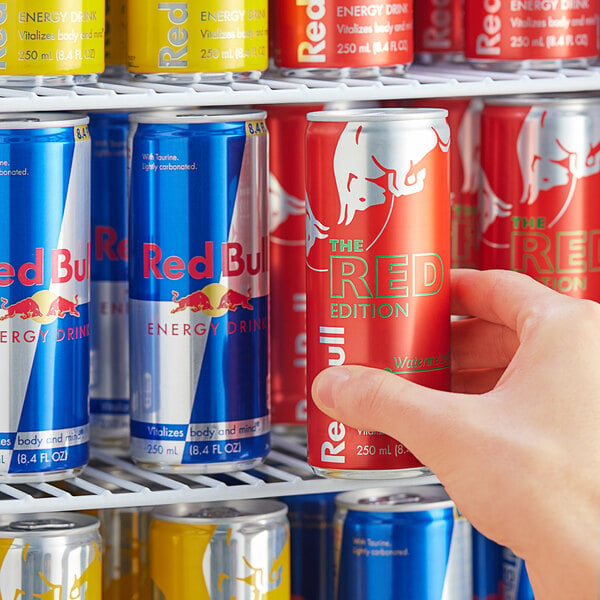 A person's hand holding a red and blue Red Bull energy drink can.