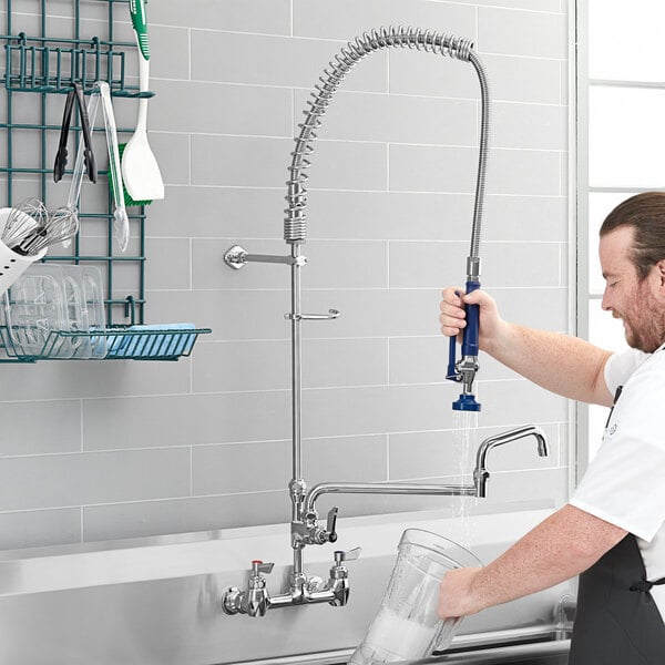 A man in an apron using a Waterloo wall-mounted pre-rinse faucet to wash dishes in a professional kitchen sink.
