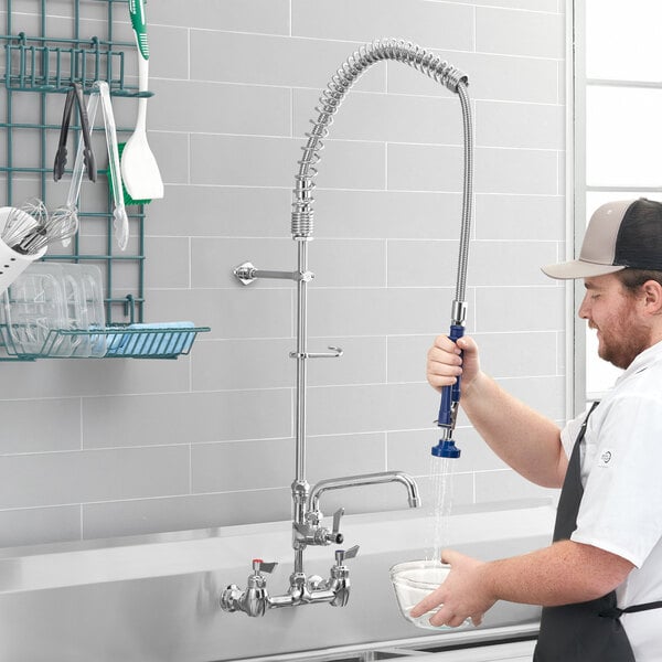 A man using a Waterloo wall-mounted pre-rinse faucet to fill a bowl with water over a counter in a professional kitchen.