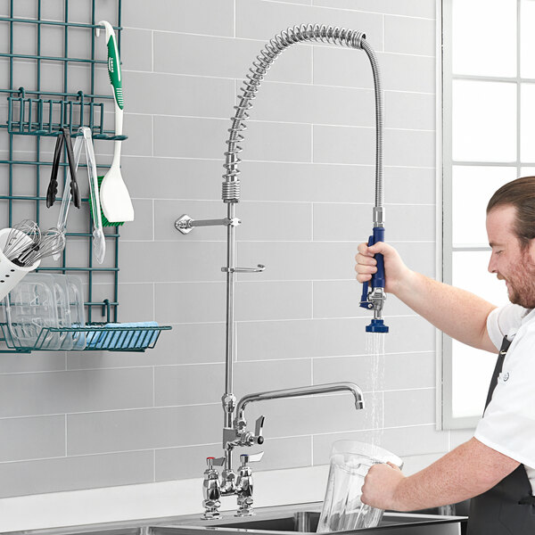 A man using a Waterloo deck-mounted pre-rinse faucet to wash a glass in a professional kitchen.