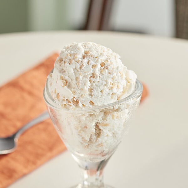 A glass with a scoop of ice cream topped with English toffee pieces.