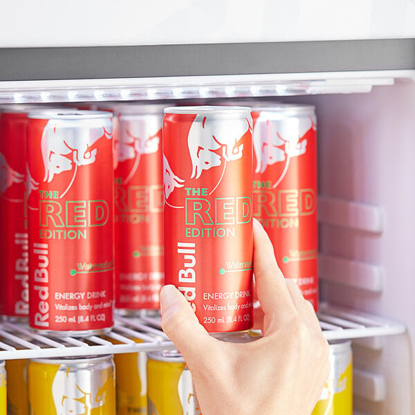 A hand taking a Red Bull Watermelon Energy Drink out of a refrigerator.