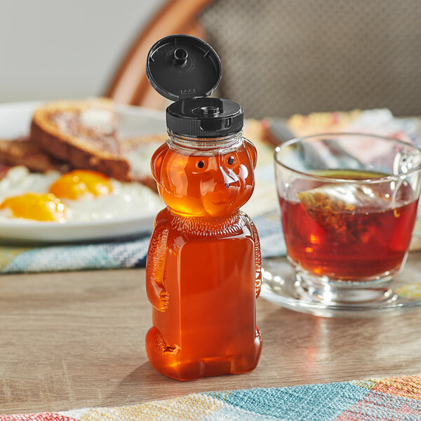 An 8 oz. bear-shaped honey bottle with a black flip top lid on a table.