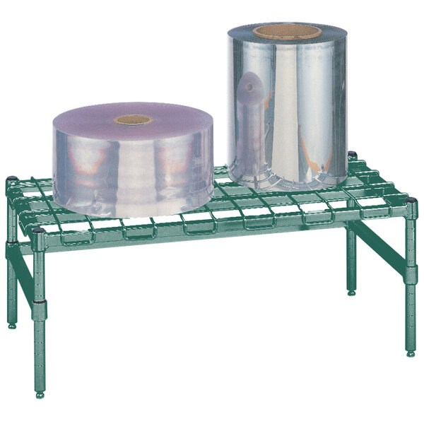 A green Metro dunnage rack with a wire mat on a table with rolls of plastic.