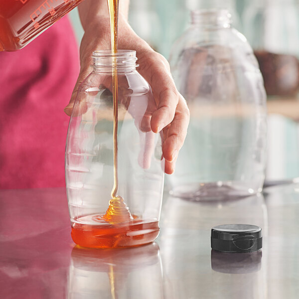 A hand pouring honey into a Classic Queenline PET Honey Bottle.